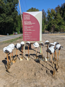 Shovels and hard hats in front of "Vance Street Homes" sign